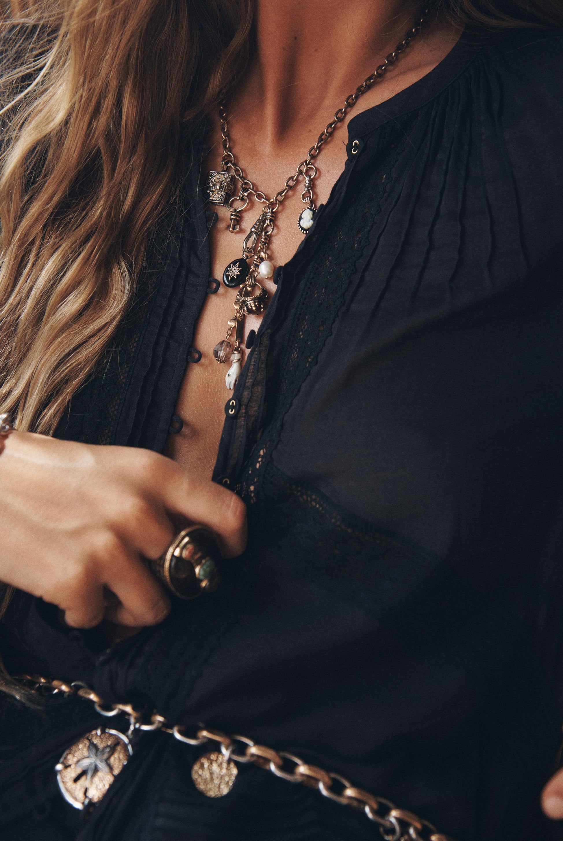 Close-up of a person wearing a black top with layered necklaces and a bracelet.