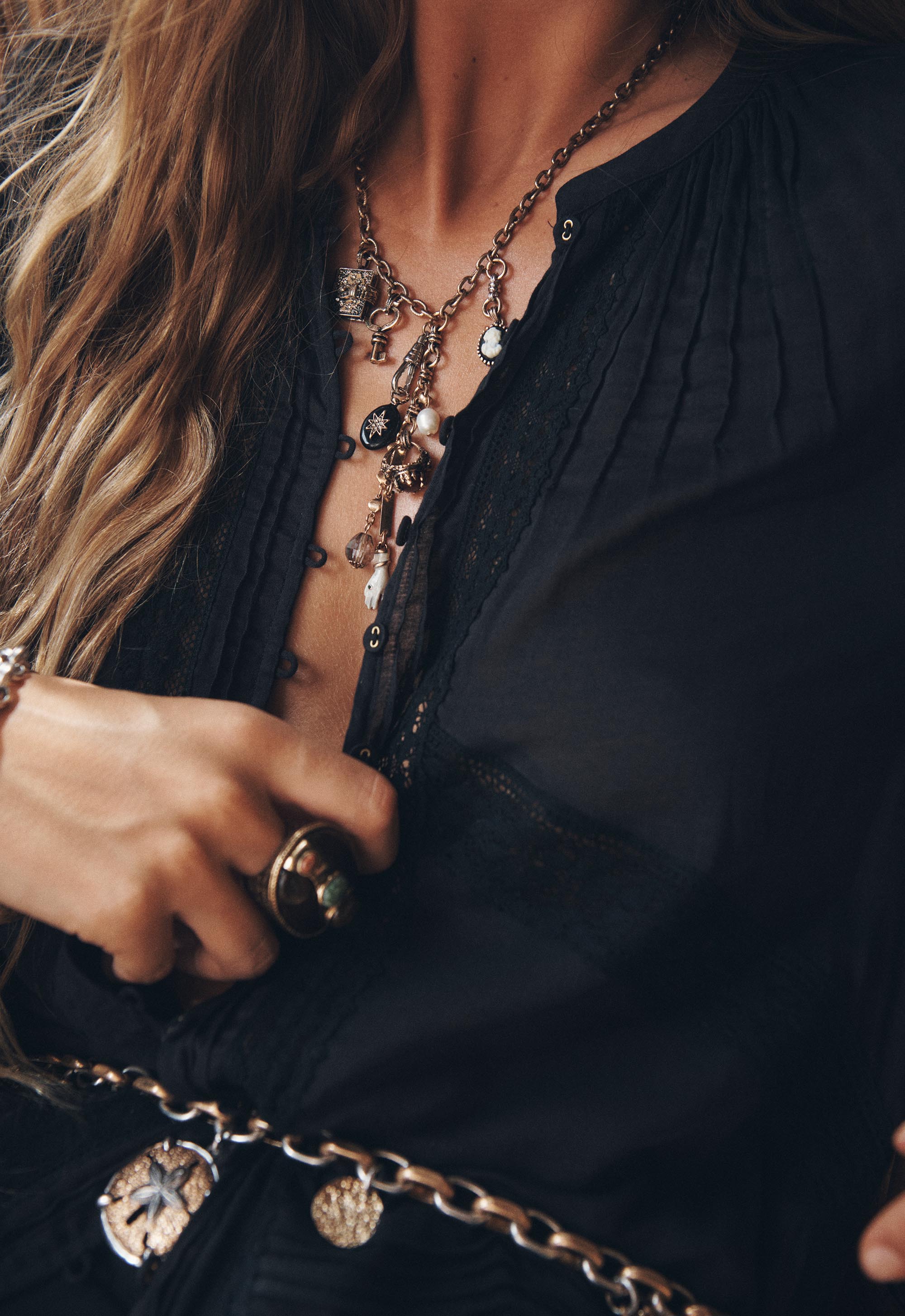 Close-up of a person wearing a black top with layered necklaces and a bracelet.