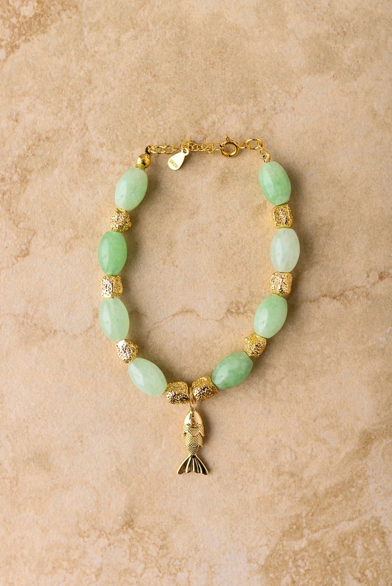 Bracelet with green beads and gold accents on a beige background