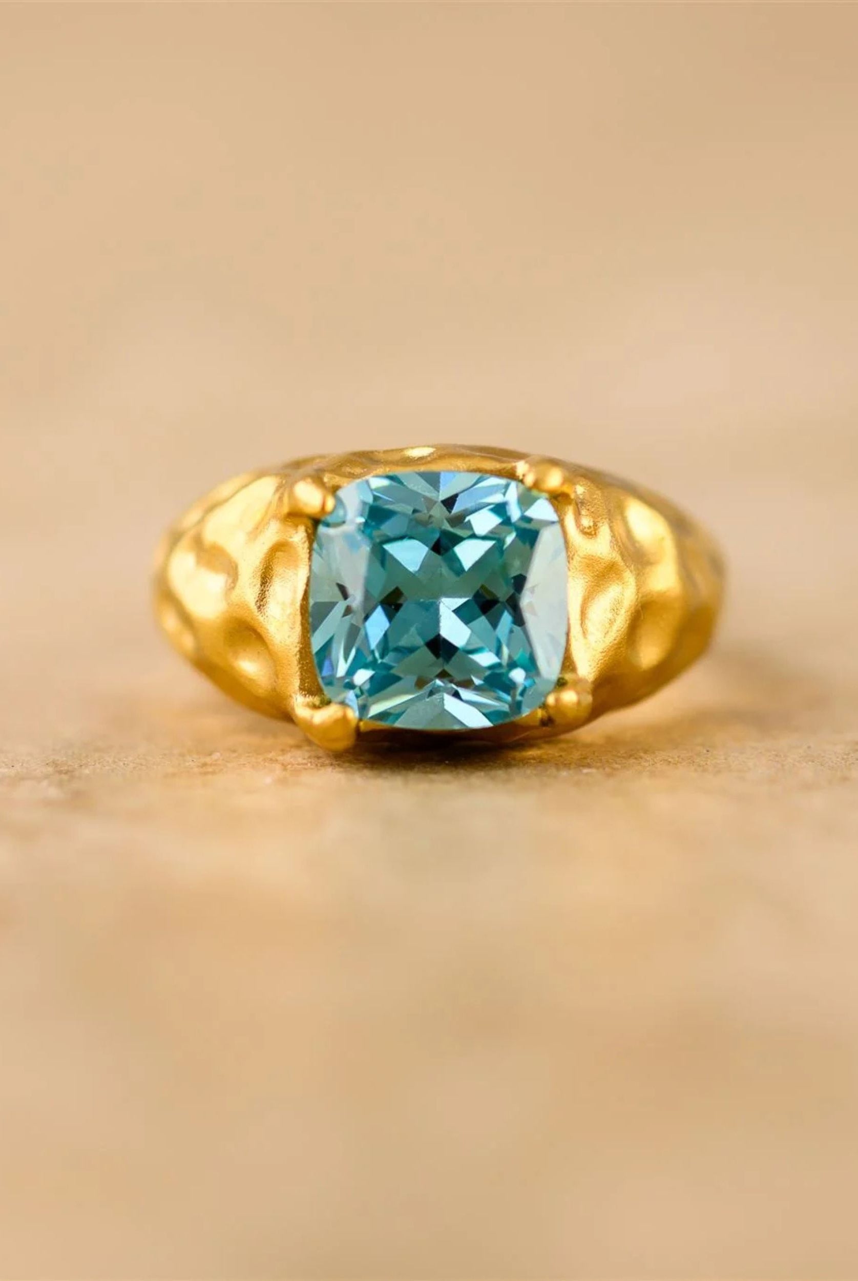 Gold ring with a blue gemstone on a beige background