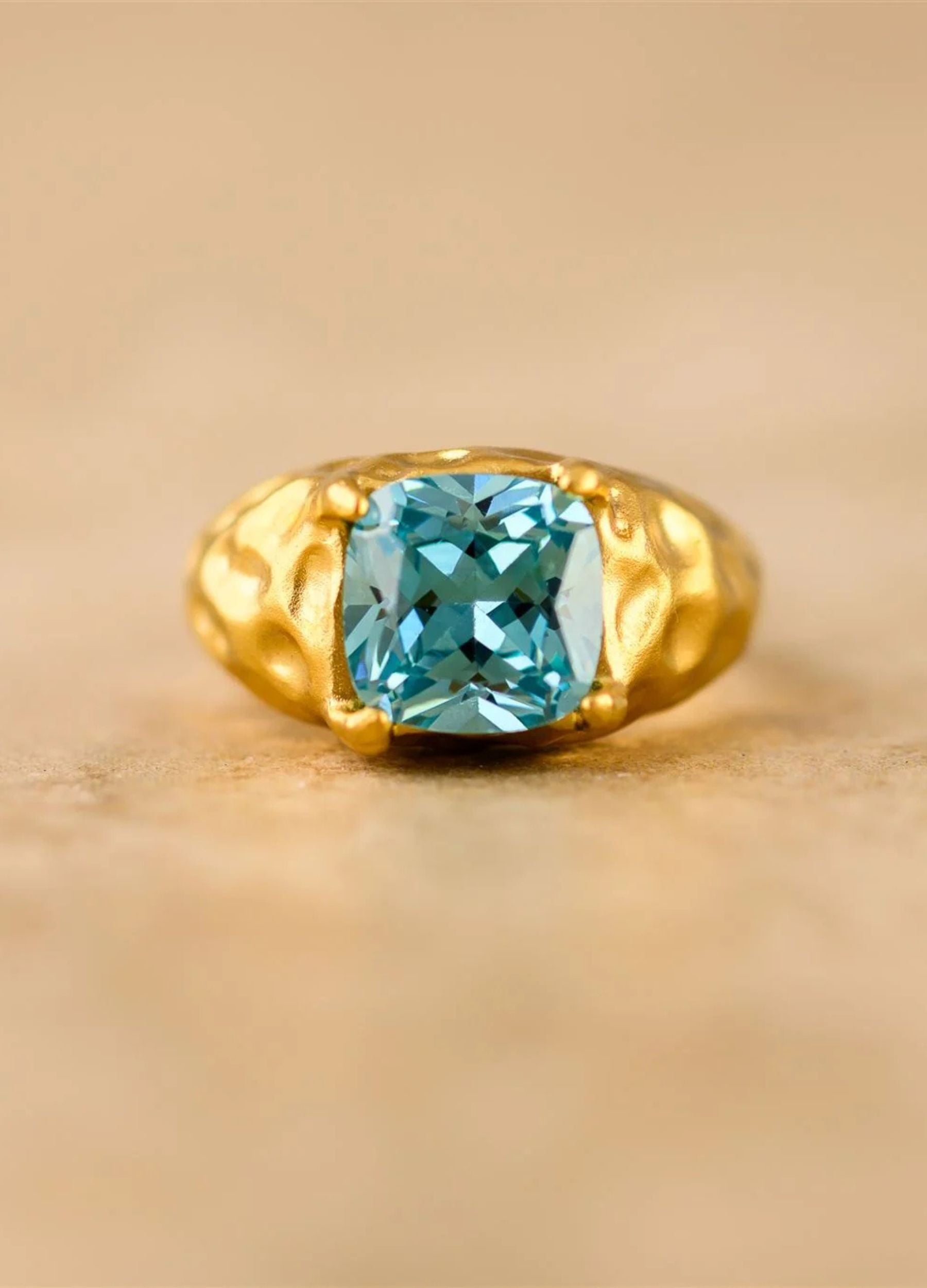 Gold ring with a blue gemstone on a beige background