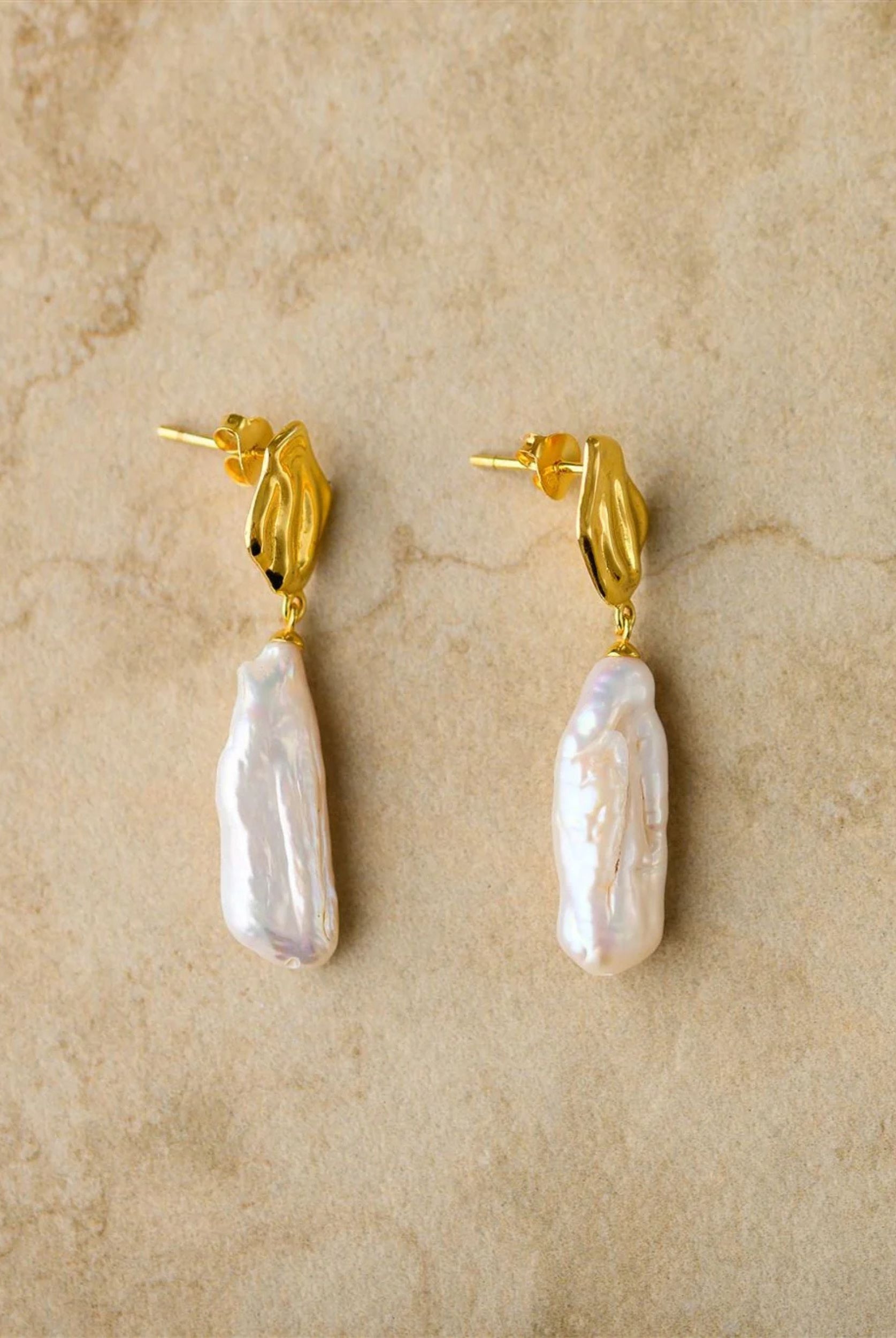 Pair of pearl earrings with gold posts on a beige background
