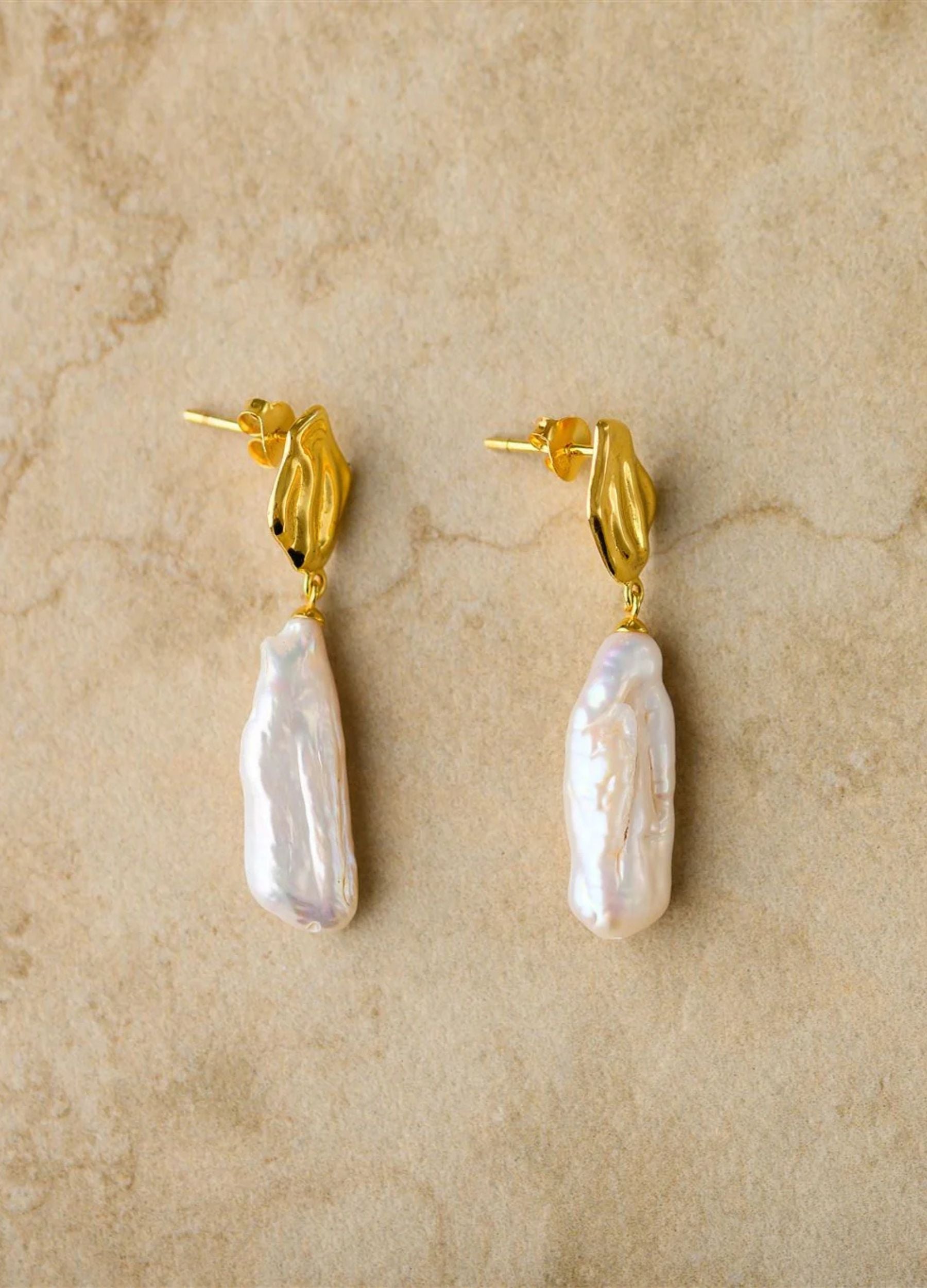 Pair of pearl earrings with gold posts on a beige background