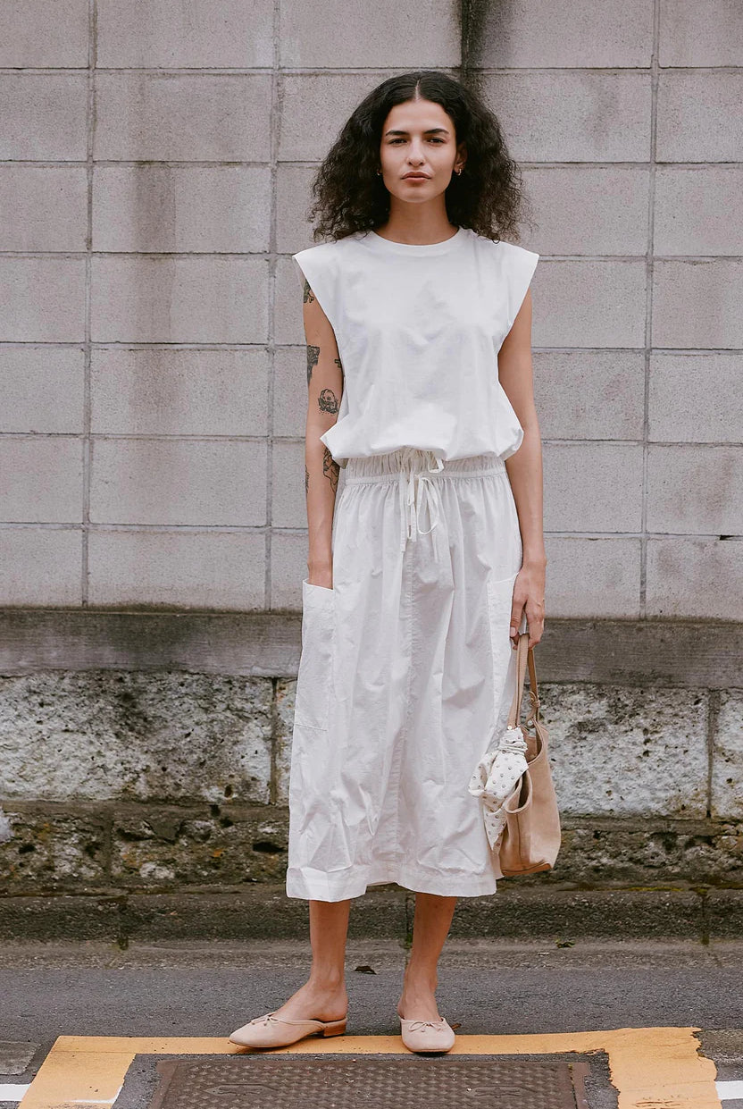 Woman wearing a white outfit standing against a textured wall.