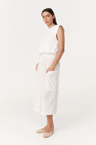 Woman wearing a white sleeveless top and pants on a white background