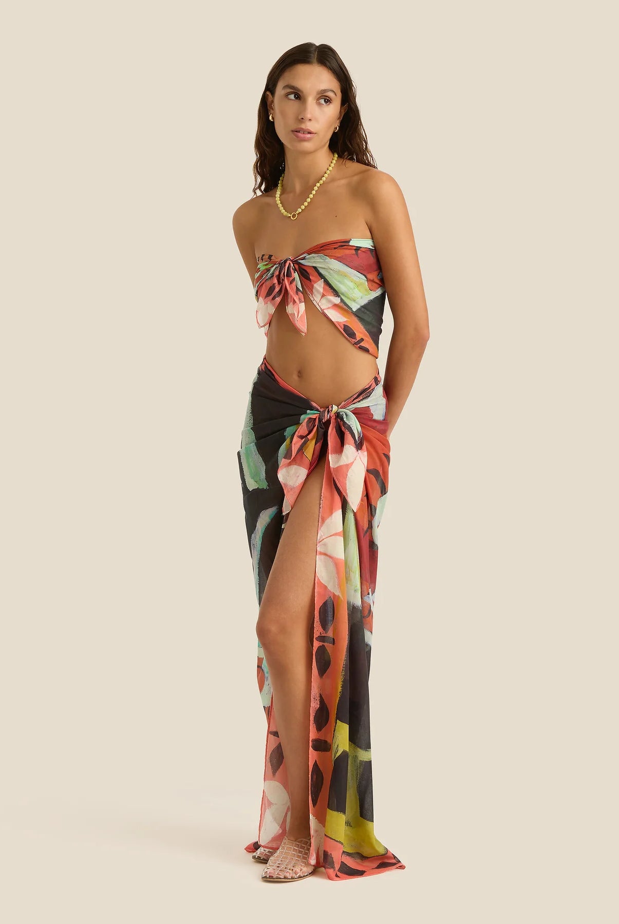 Woman wearing a floral one-shoulder top and long skirt on a beige background