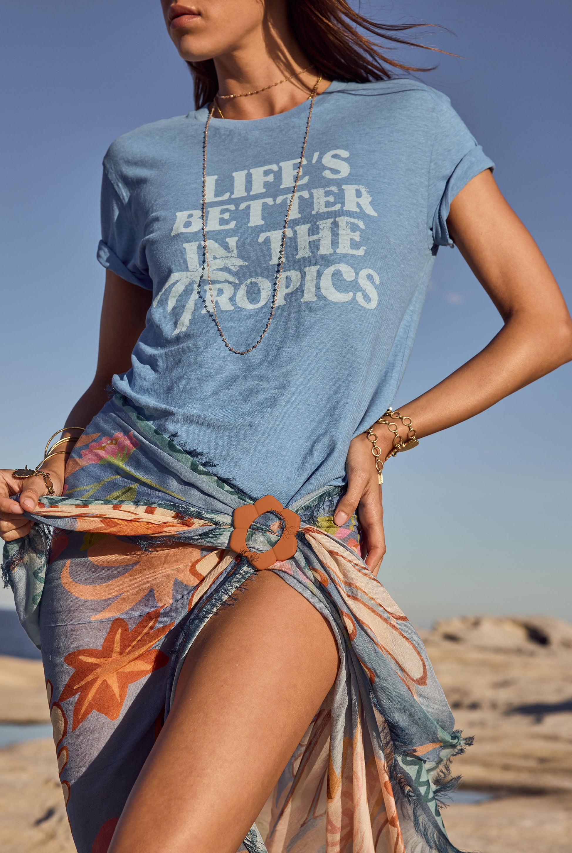 Person wearing a blue t-shirt with 'Life's Better in the Tropics' text on a beach.