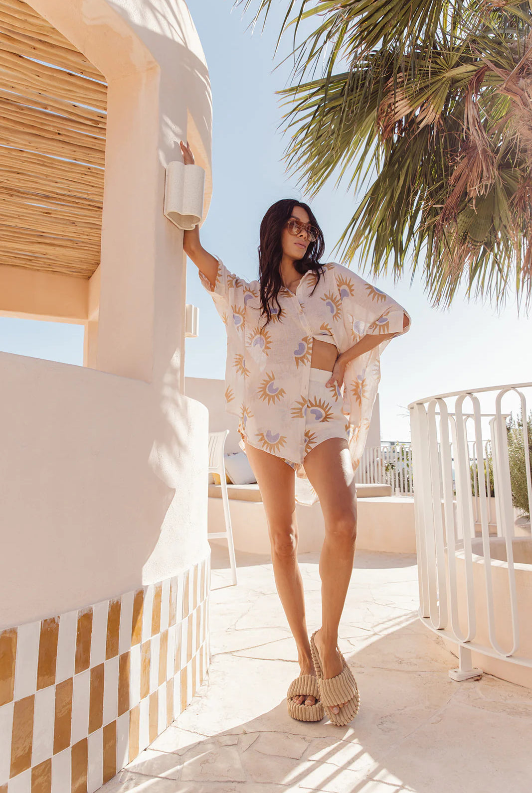 Woman in a floral dress standing on a balcony with palm trees in the background