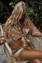 Woman wearing a floral shirt and wrap skirt sitting on a chair with greenery in the background