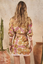 Woman wearing a patterned outfit standing in front of a textured wall with a cactus and vase.