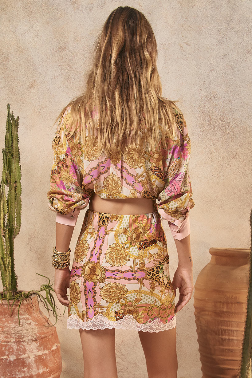 Woman wearing a patterned outfit standing in front of a textured wall with a cactus and vase.