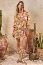 Woman in a patterned outfit standing among cacti and decorative pots.