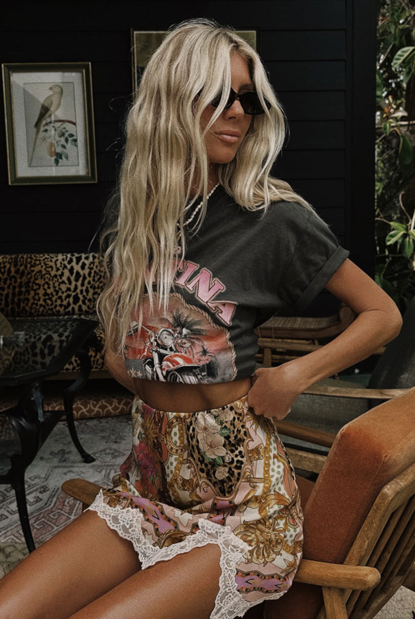 Woman wearing a graphic t-shirt and patterned skirt sitting on a chair.