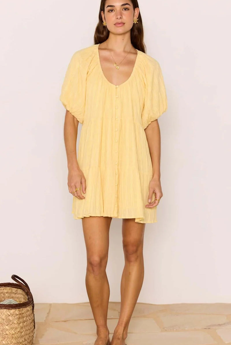 Woman wearing a yellow dress standing against a plain background