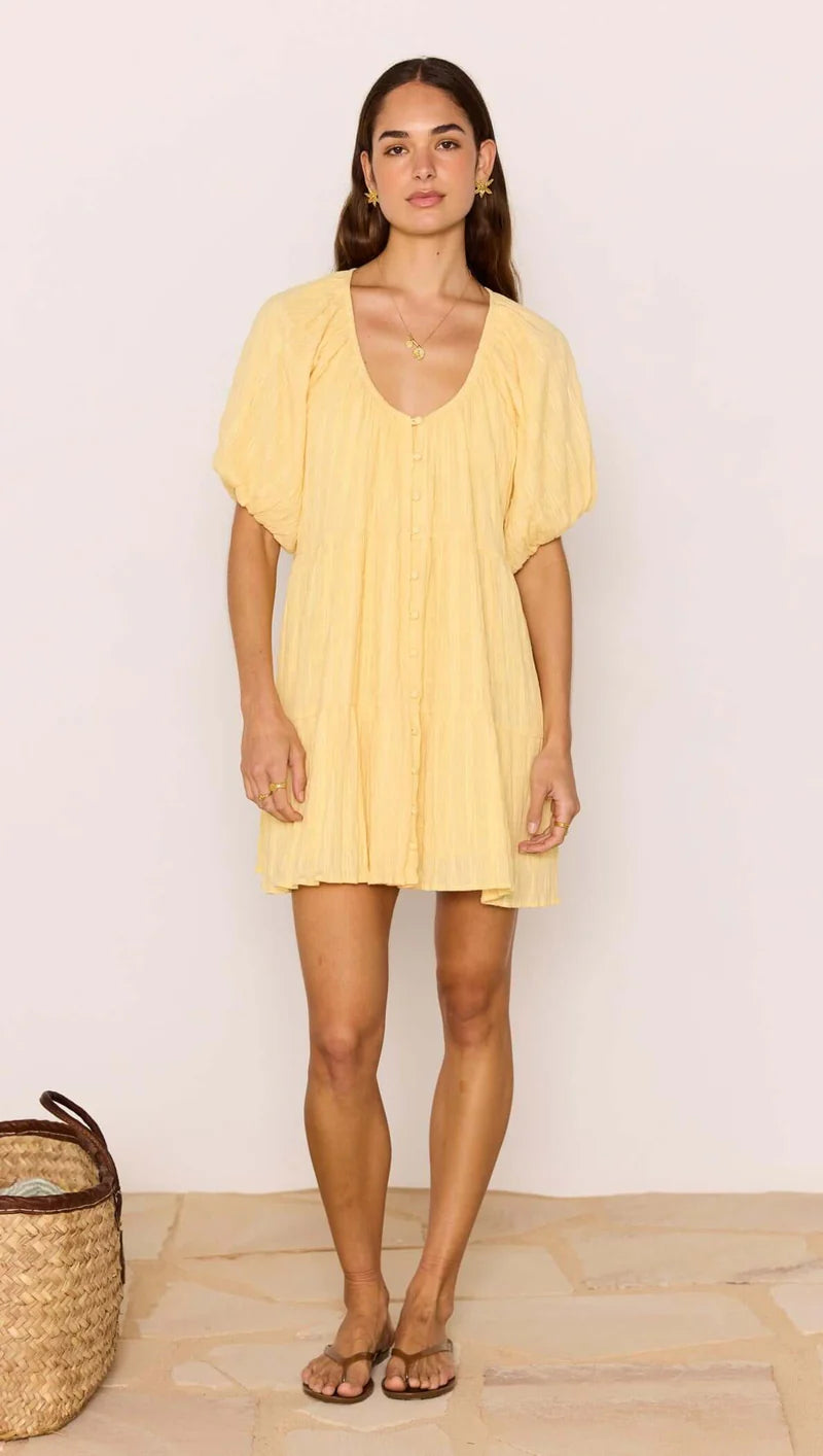 Woman wearing a yellow dress standing against a plain background