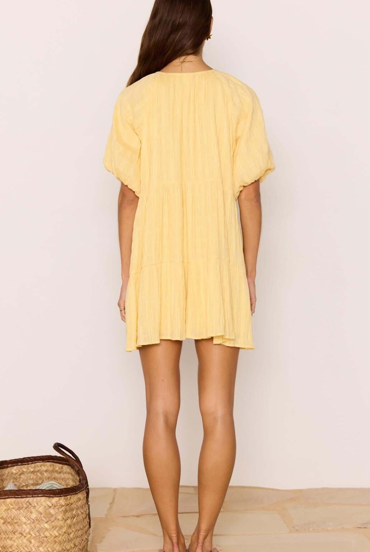 Woman wearing a yellow dress standing against a plain background