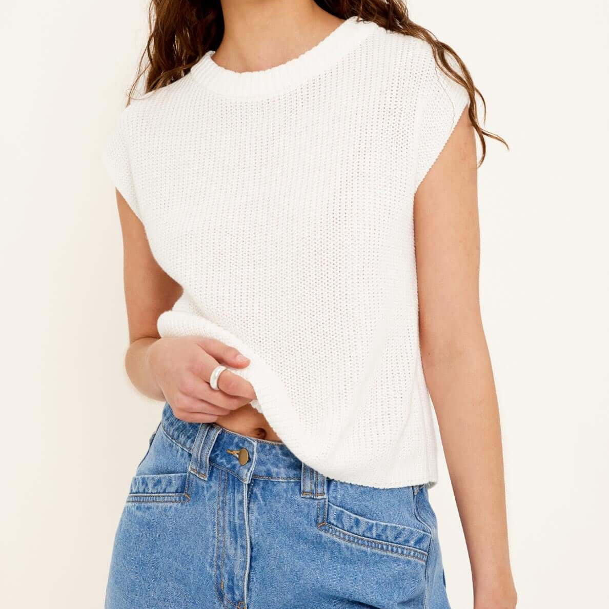 Woman wearing a white sleeveless top and blue denim shorts on a plain background