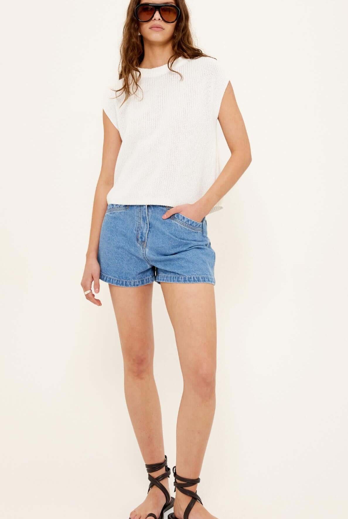 Woman wearing a white sleeveless top and blue denim shorts on a white background