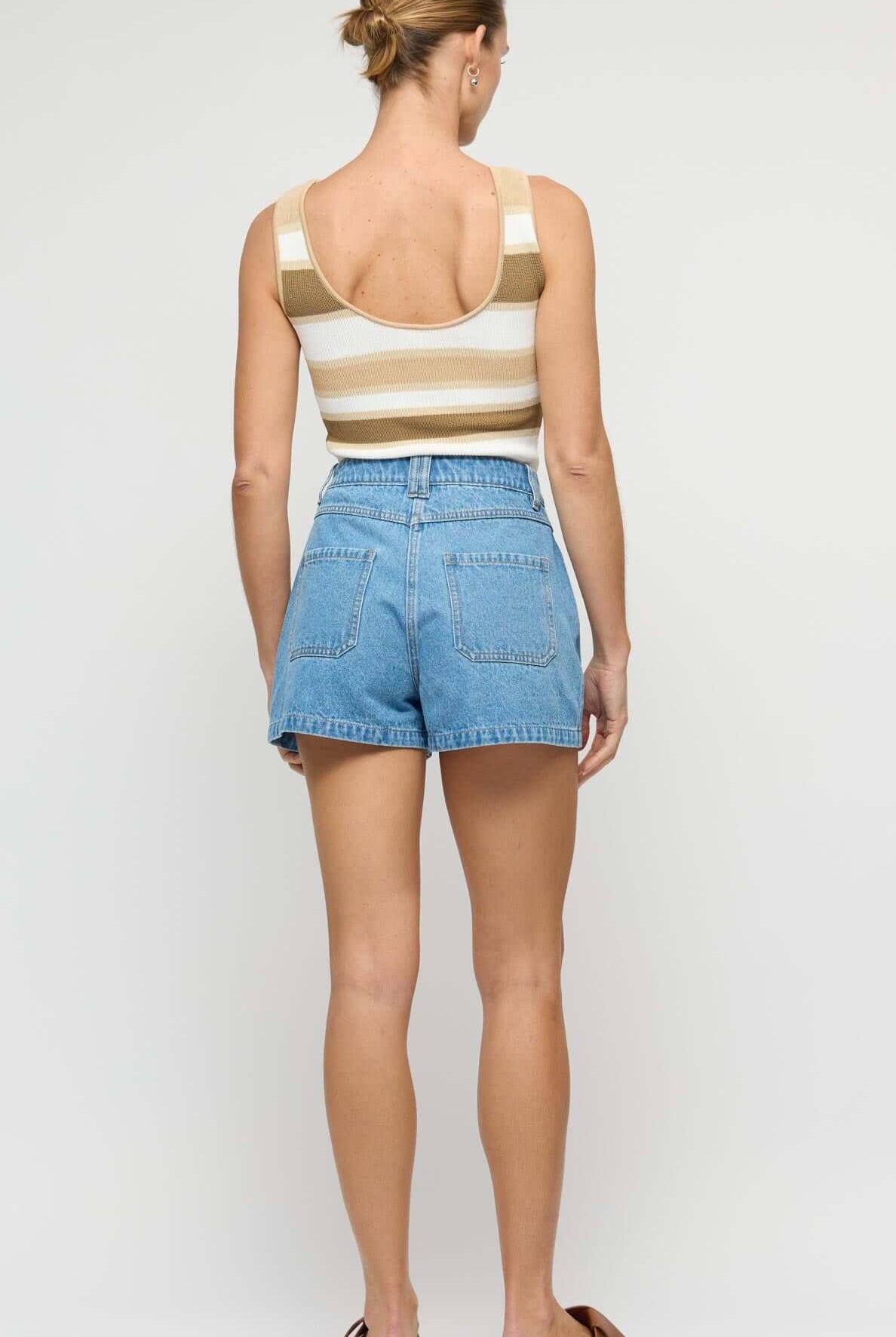 Woman wearing a striped tank top and denim shorts on a plain background