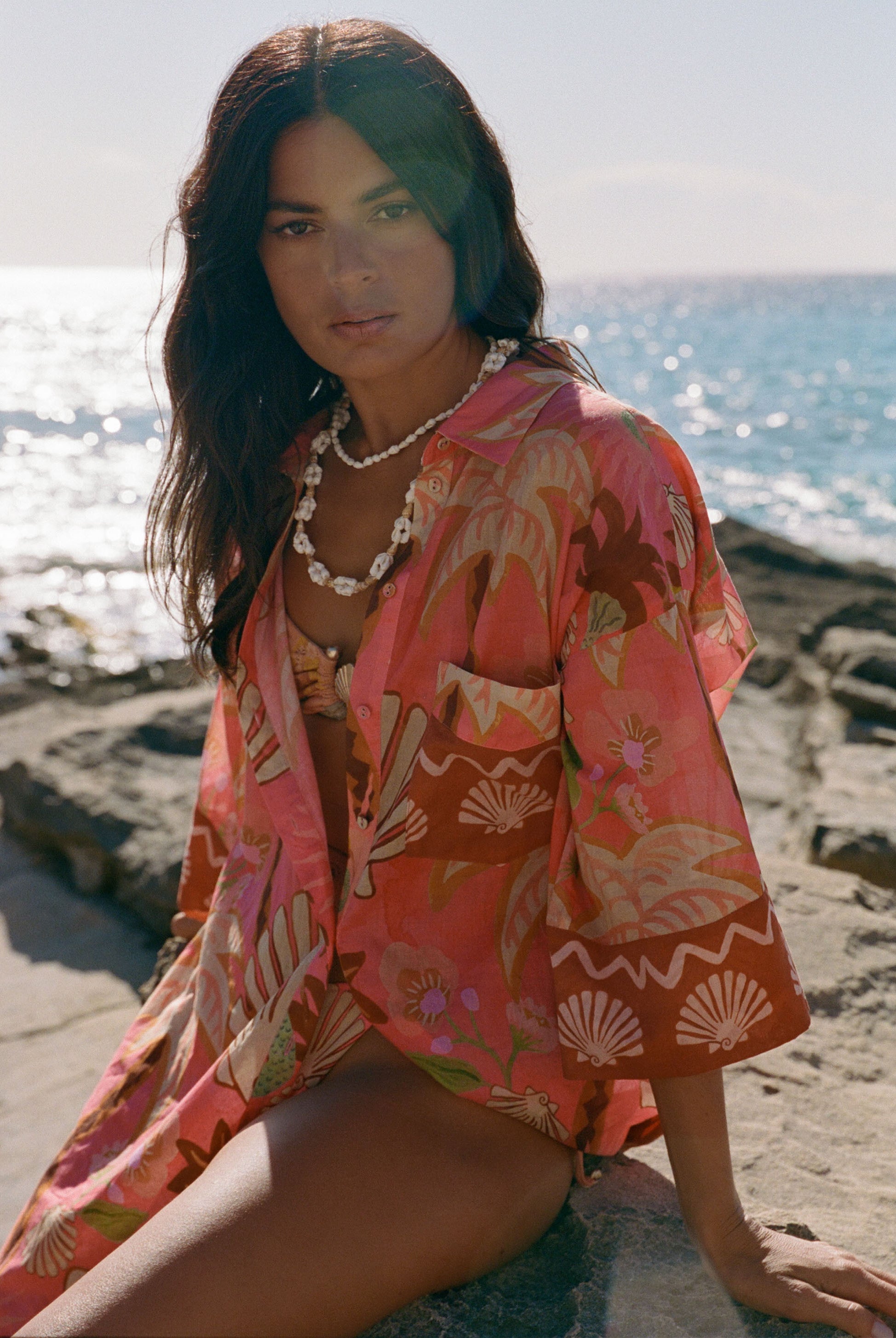 Woman in a pink floral kimono sitting on a beach with ocean in the background