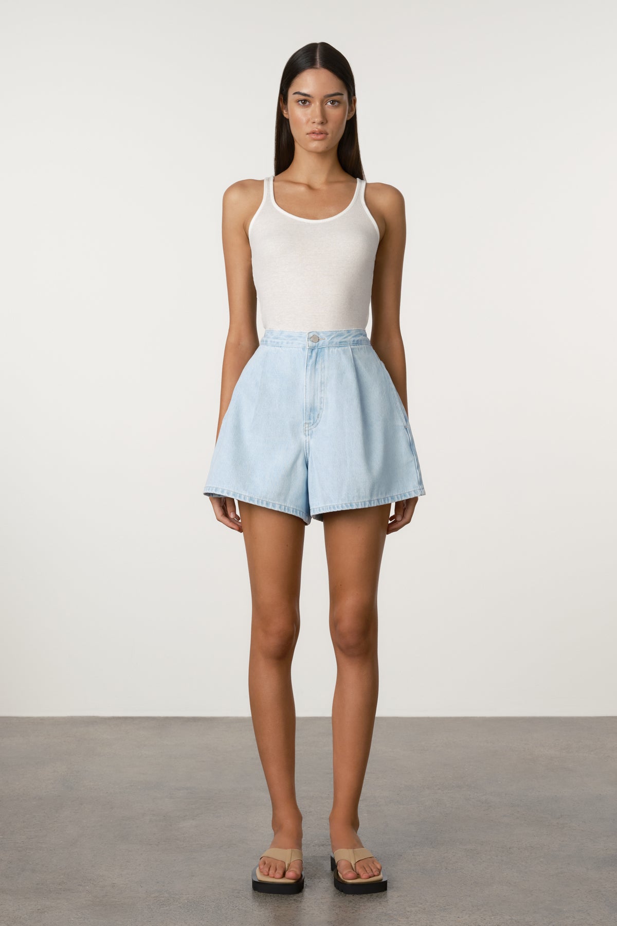 Woman wearing a white tank top and light blue shorts on a plain background