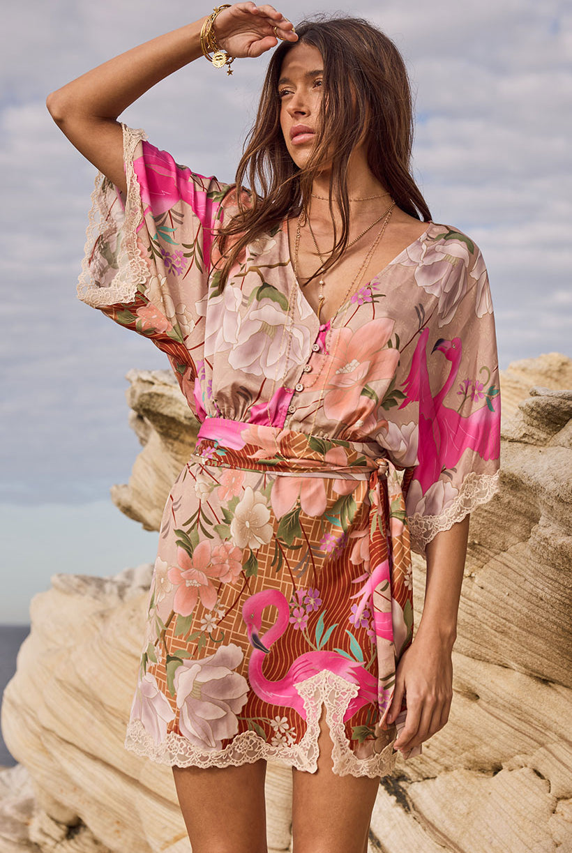 Woman wearing a floral and flamingo-patterned dress on a rocky beach.