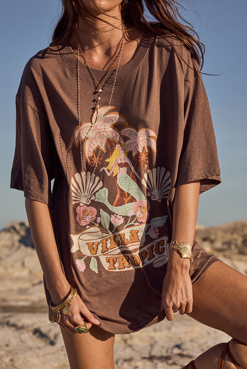 Person wearing a brown t-shirt with a mermaid graphic design in a desert setting