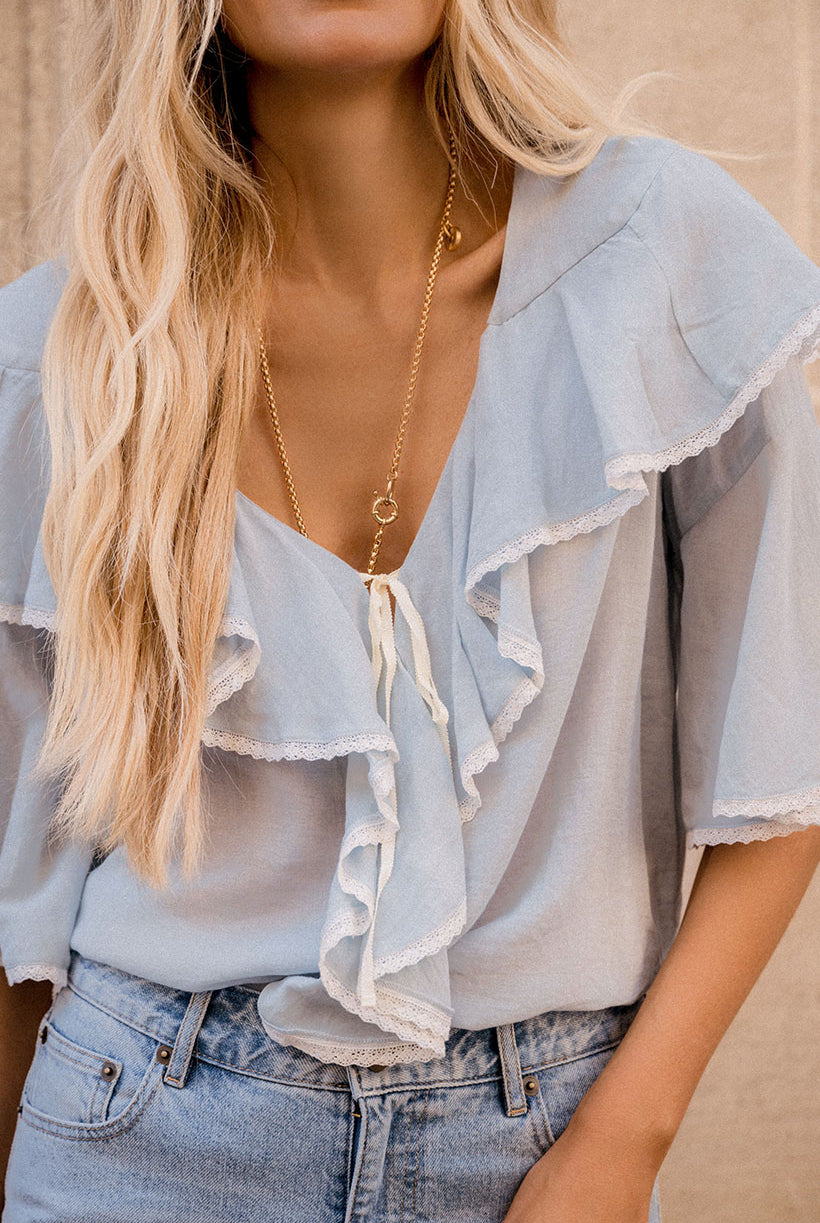 Light blue blouse with ruffled details and denim jeans worn by a person.