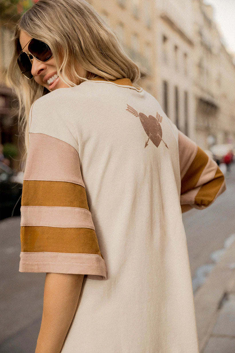 Woman wearing a beige and brown striped dress with a pattern on the back, walking on a street.