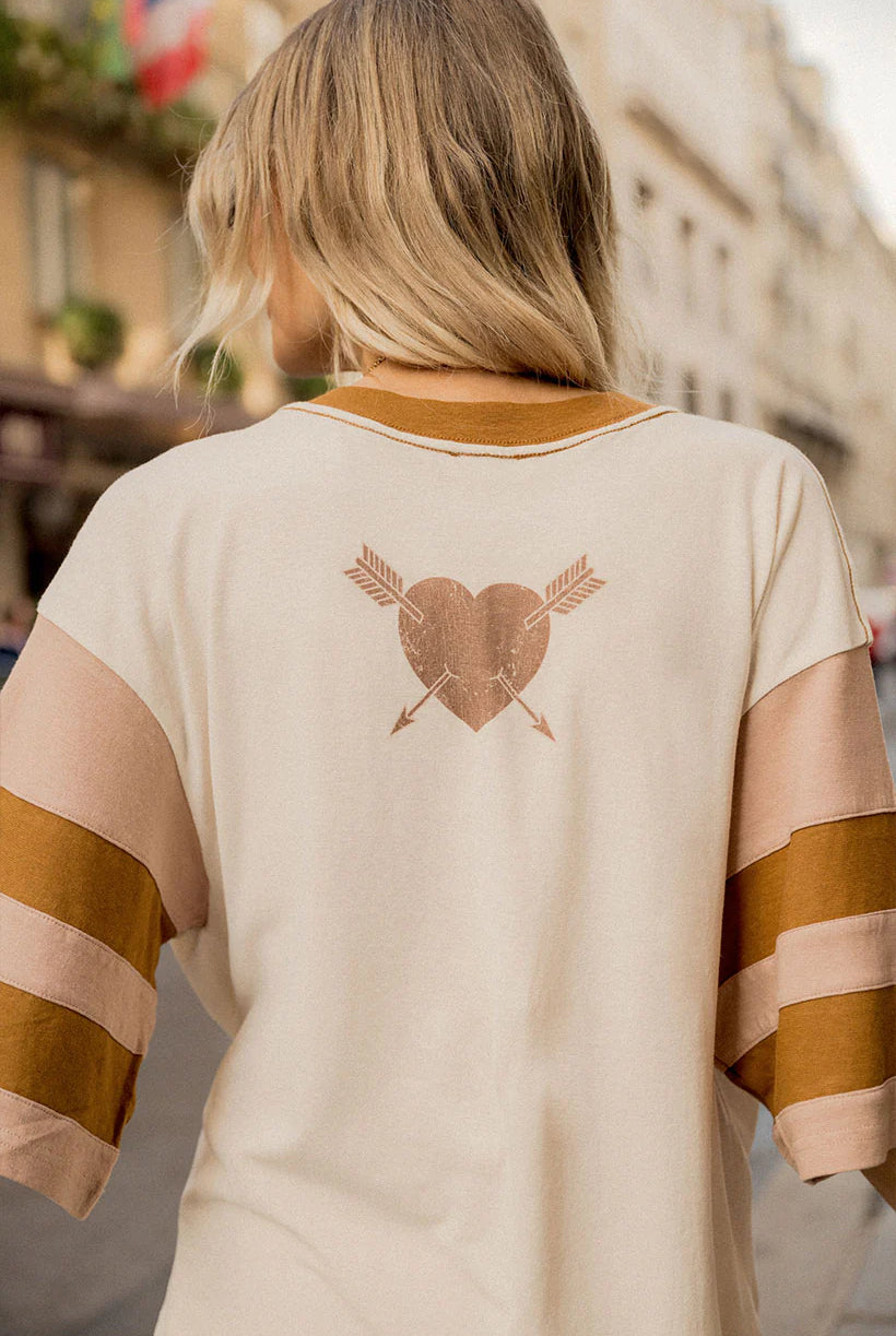 Person wearing a beige and brown striped shirt with a heart and arrow design on the back, standing in an urban setting.