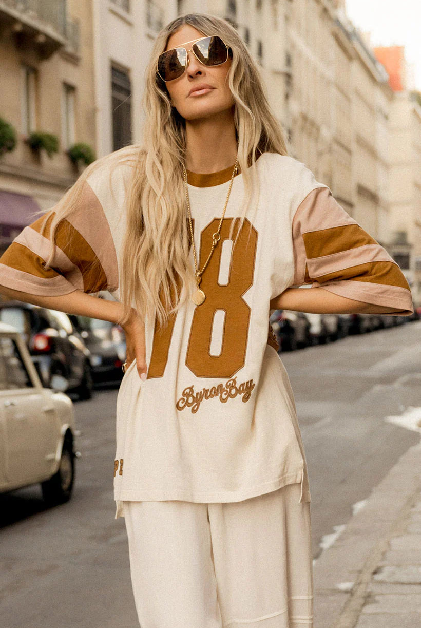 Woman wearing a beige and brown striped shirt with large numbers on a city street.
