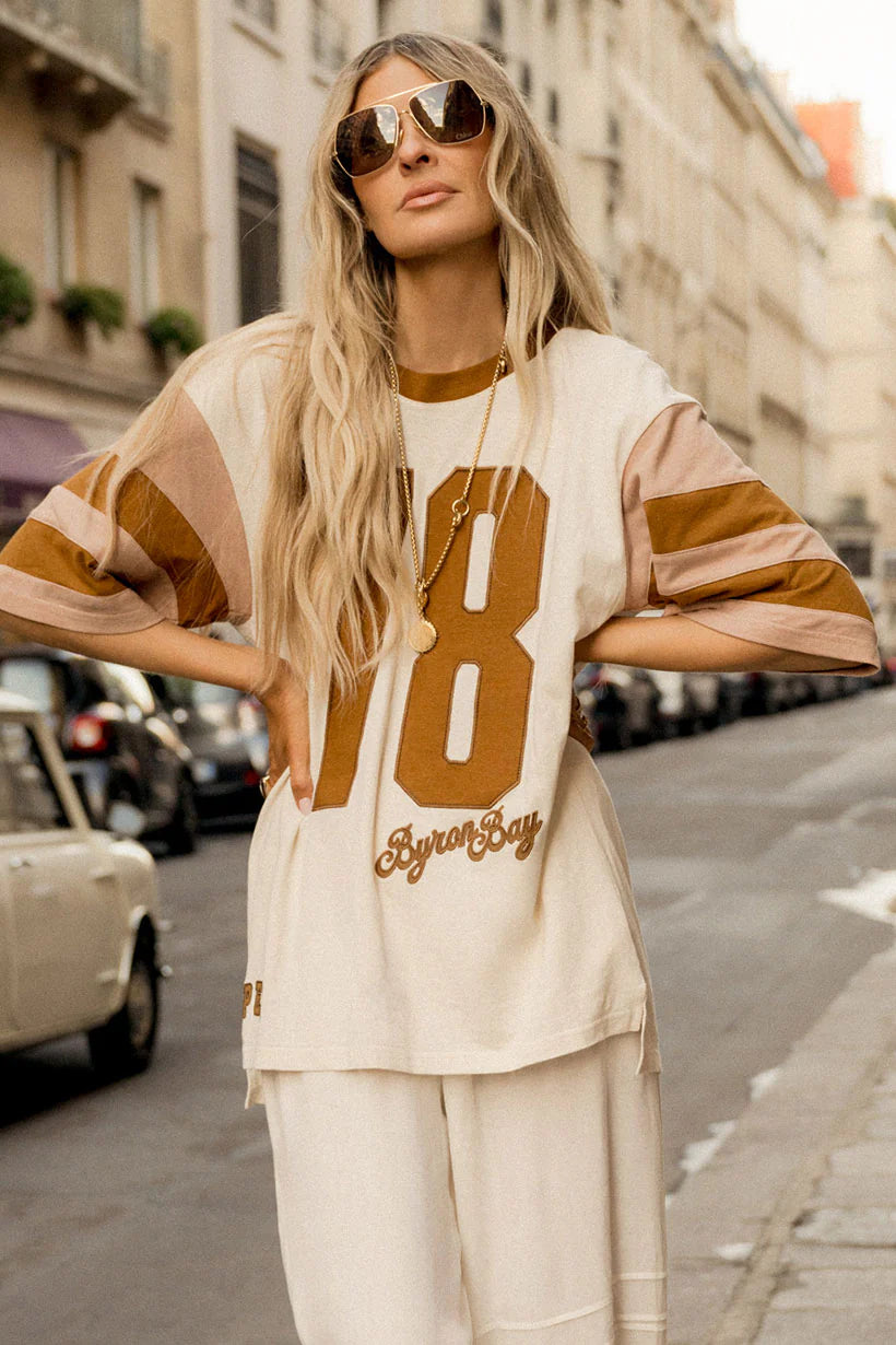Woman wearing a beige and brown striped shirt with large numbers on a city street.
