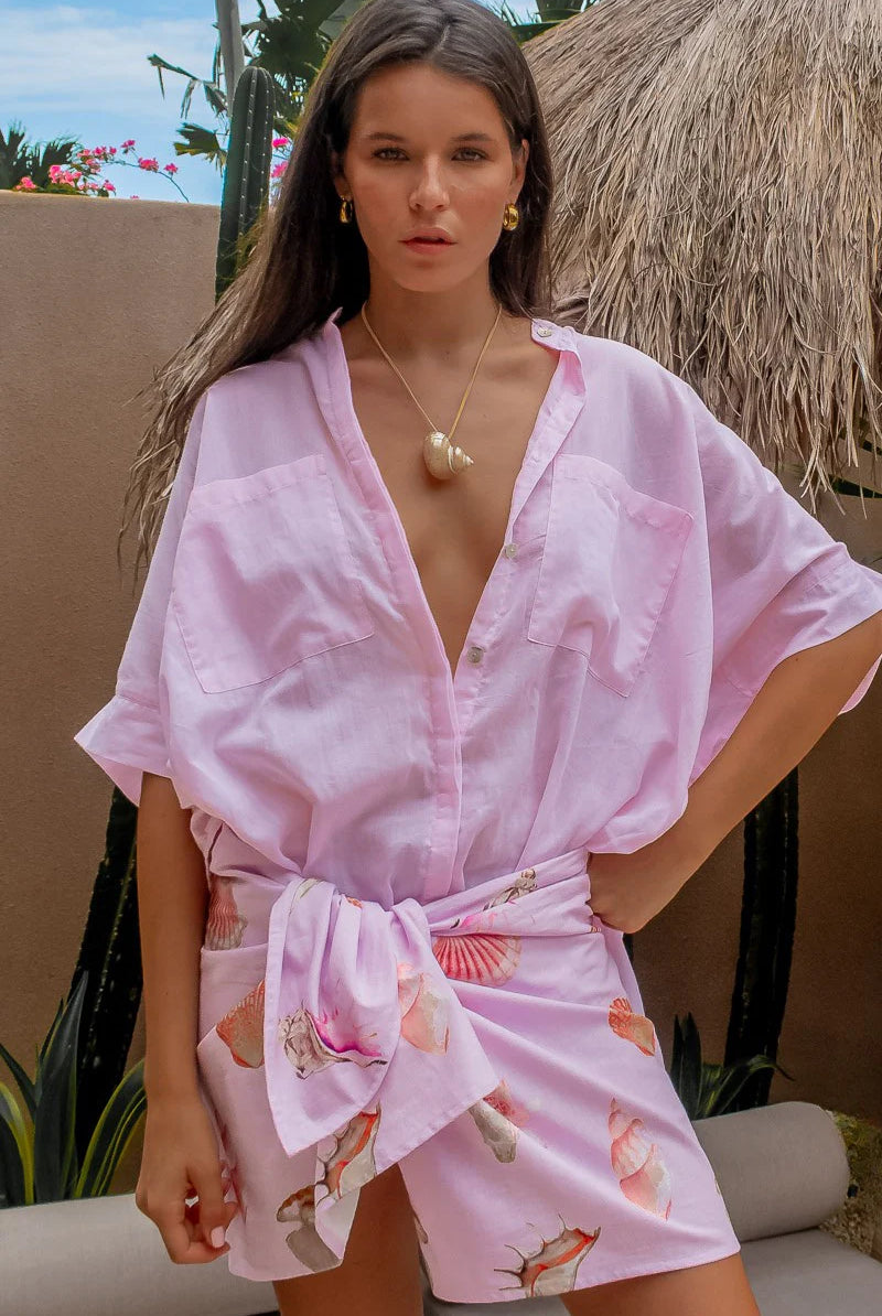 Woman wearing a pink kimono-style pink blouse with floral patterns outdoors.