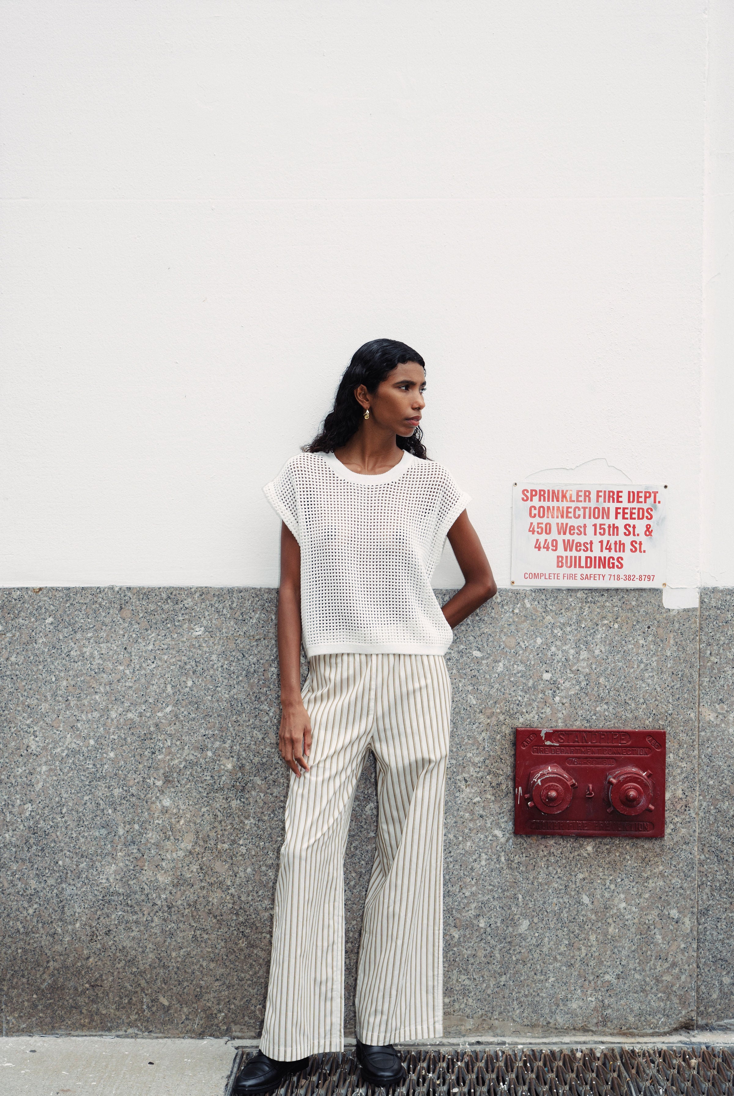 Girl wearing stripe pants against a wall.