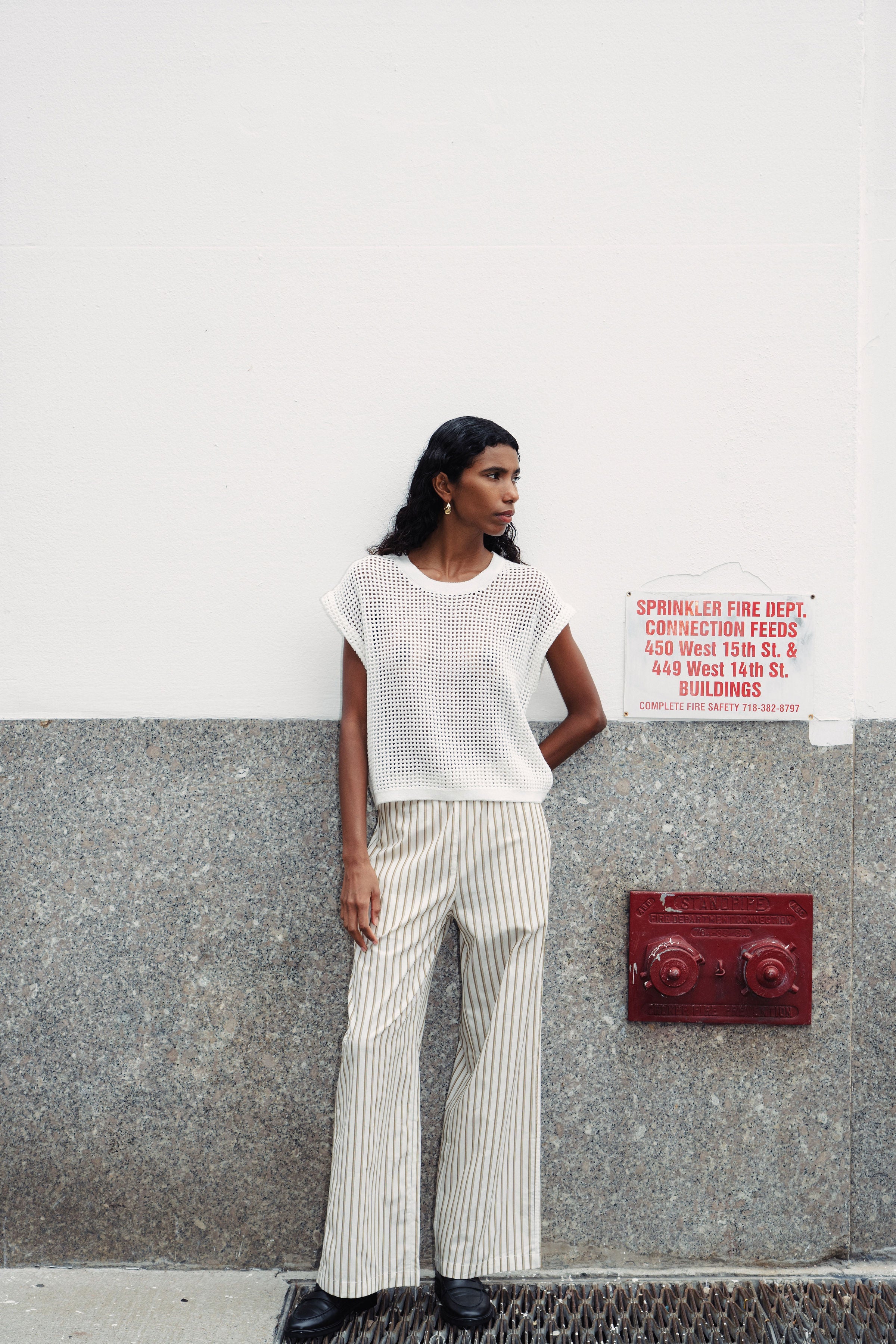 Girl wearing stripe pants against a wall.