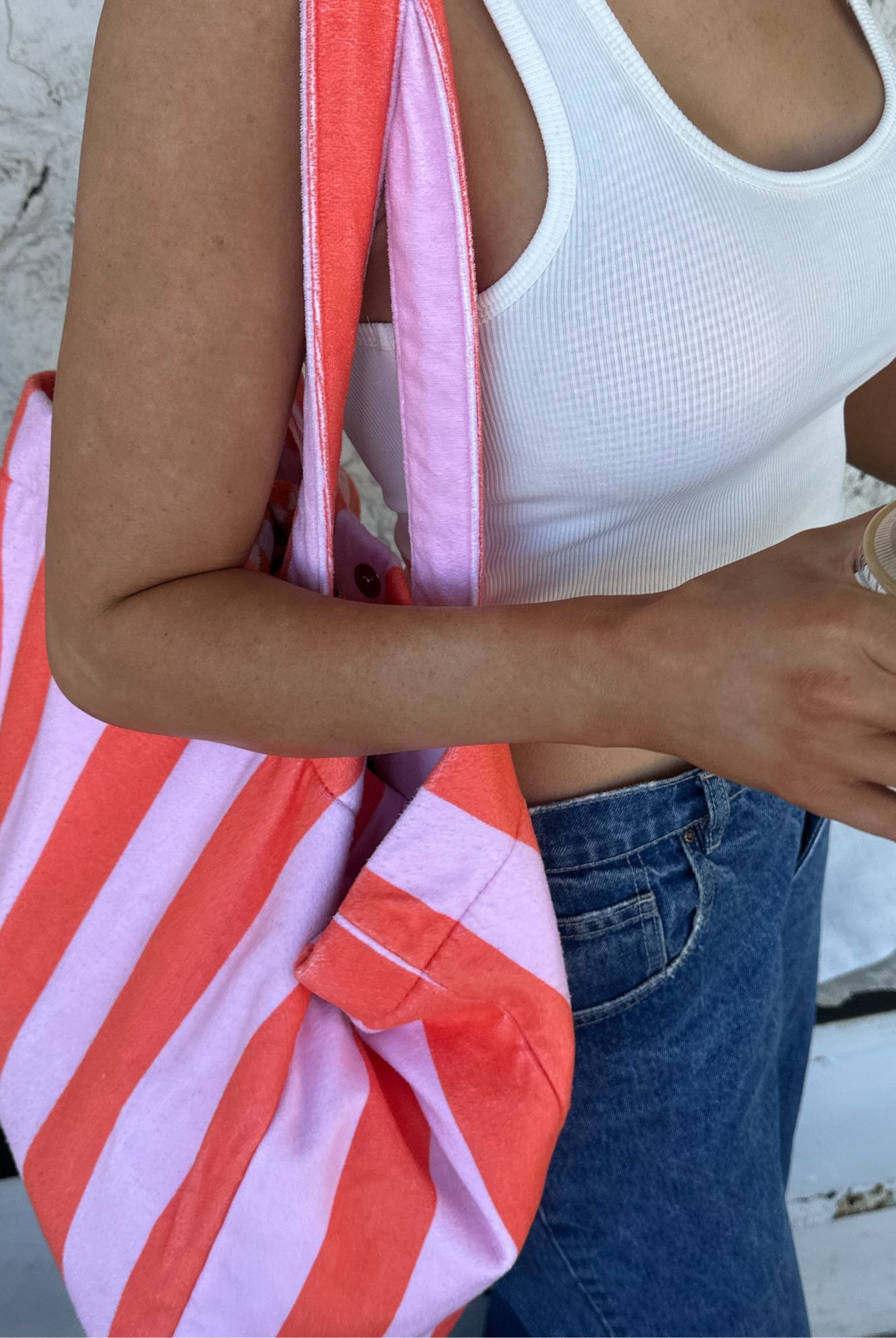 Person holding a orange and pink striped bag with a white top and blue jeans.