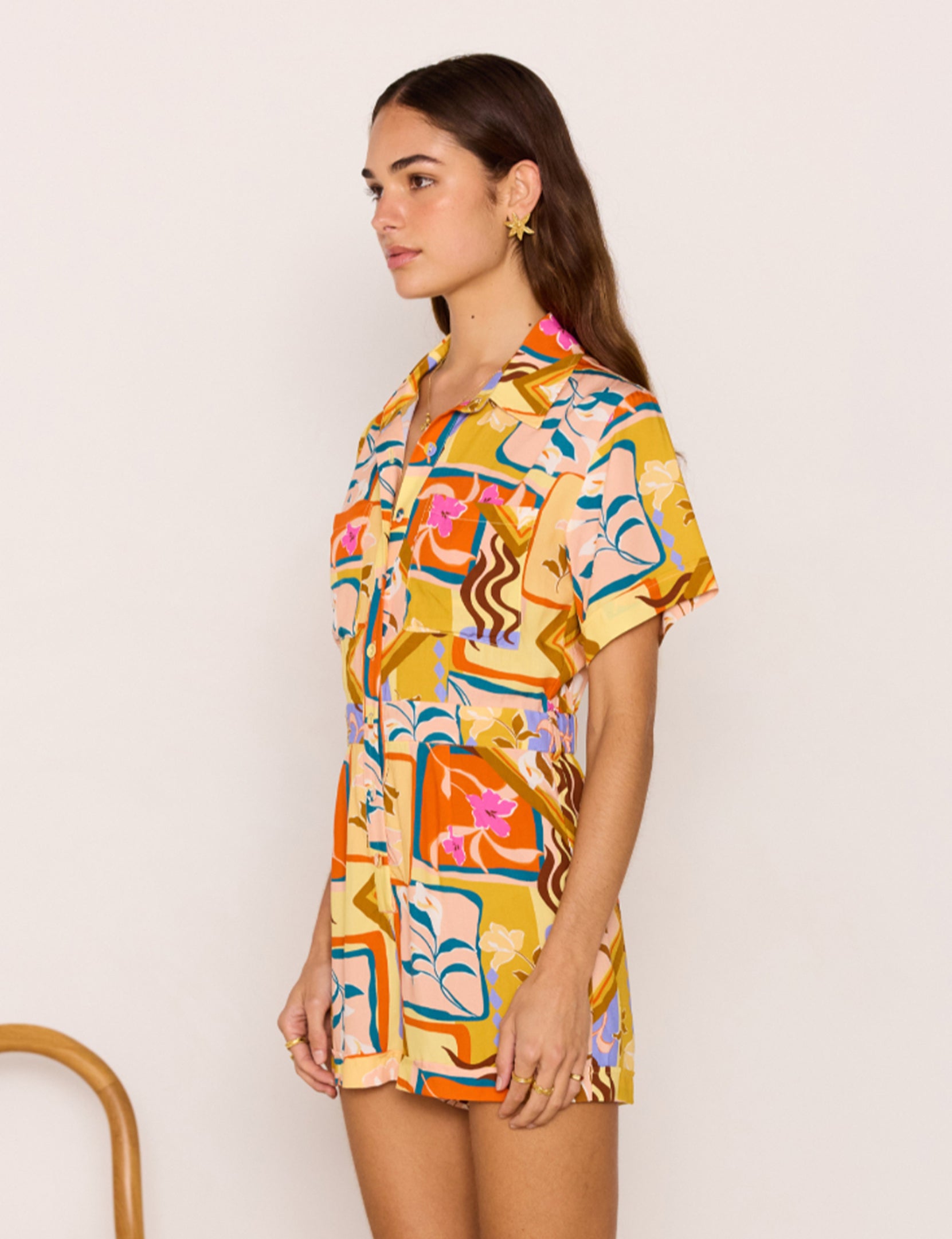 Woman wearing a colorful patterned shirt dress against a plain background
