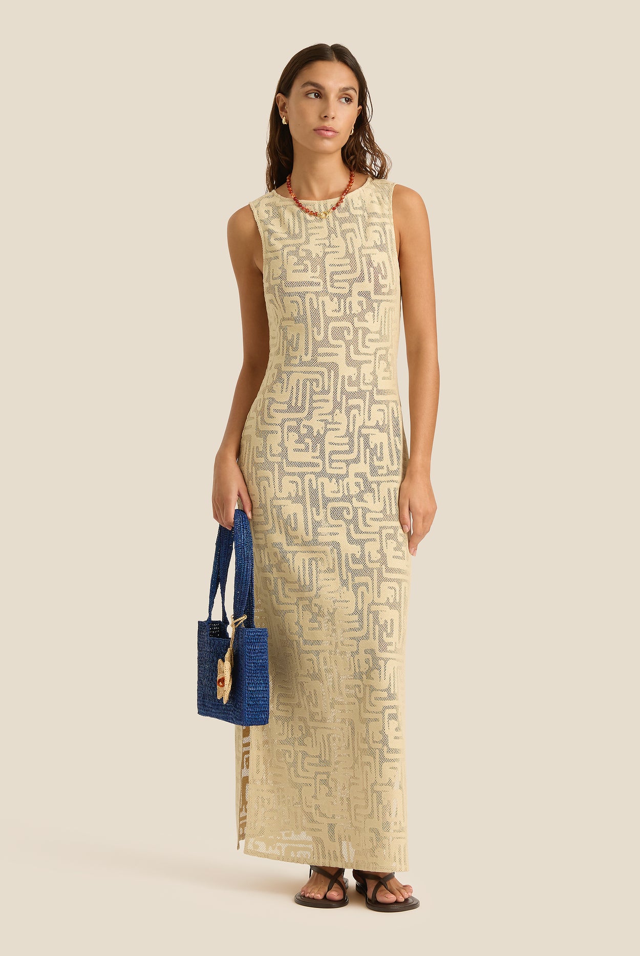 Woman wearing a beige patterned dress holding a blue handbag on a beige background