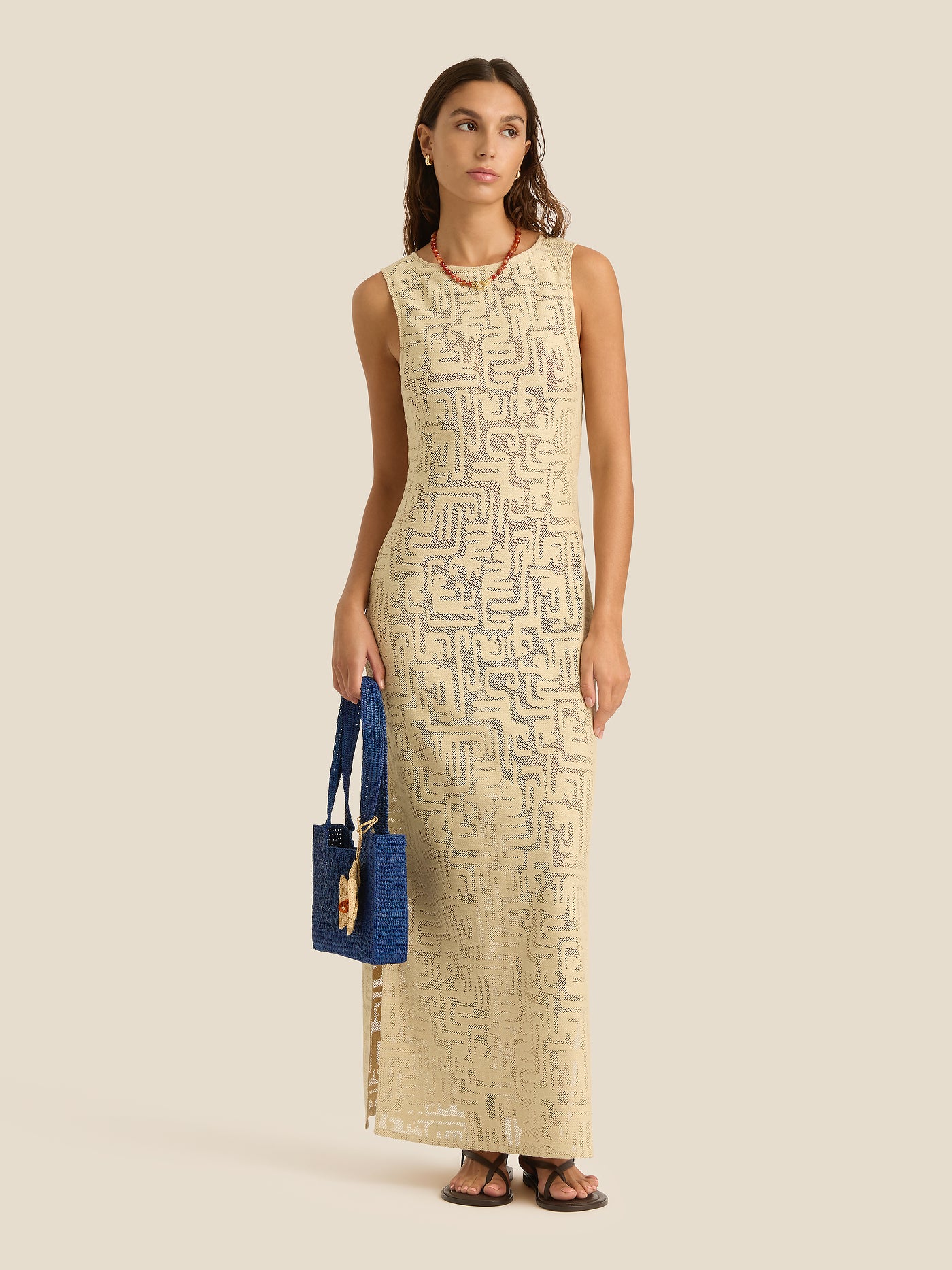 Woman wearing a beige patterned dress holding a blue handbag on a beige background