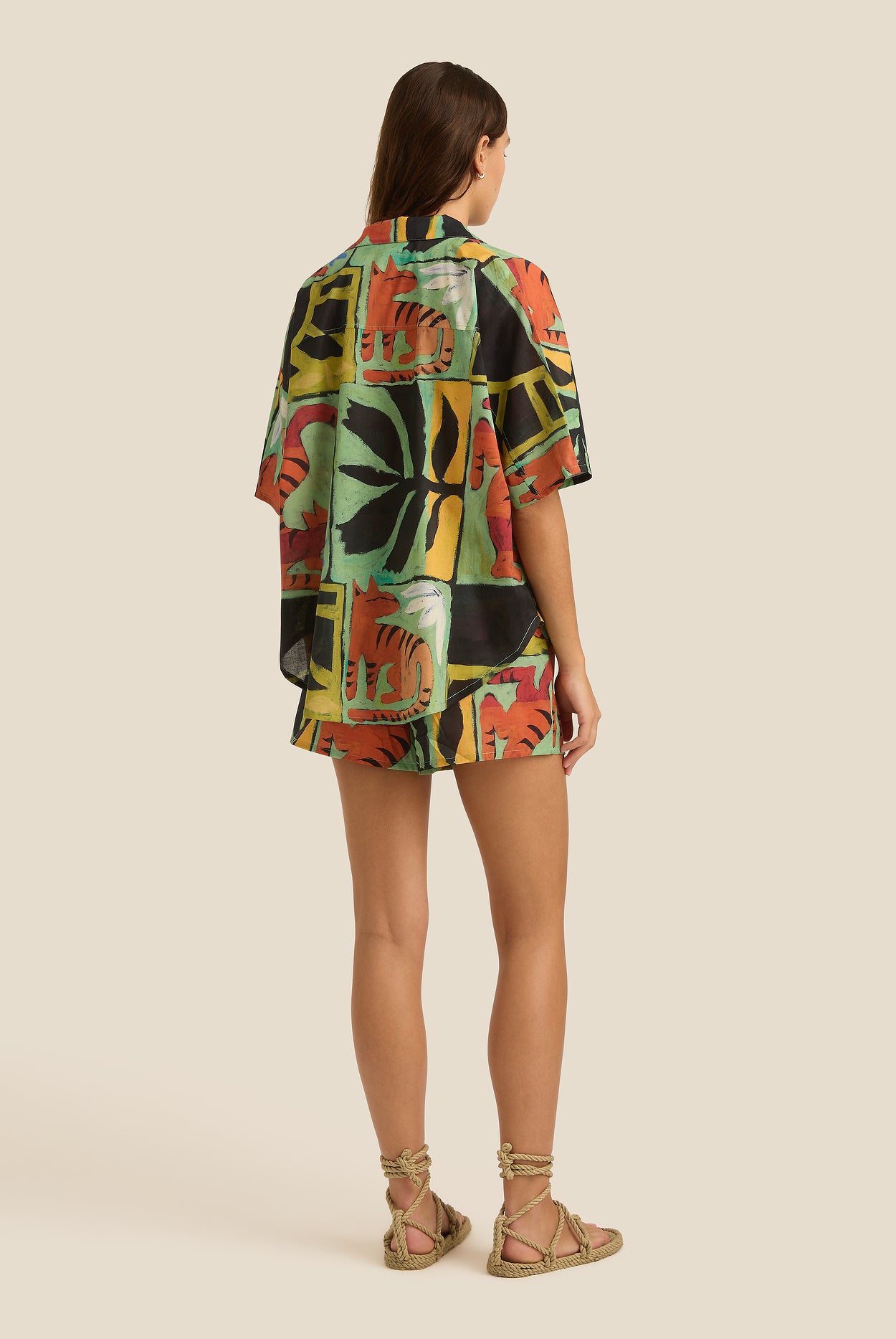 Woman wearing a colorful patterned shirt and shorts on a beige background