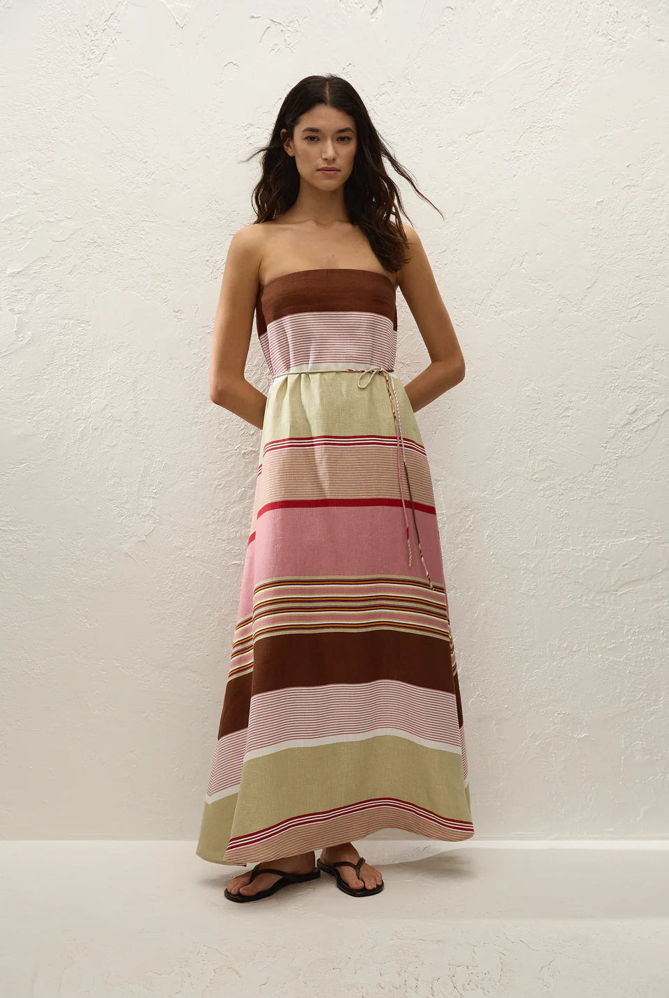 Woman wearing a strapless, long, multicolored striped dress against a white background
