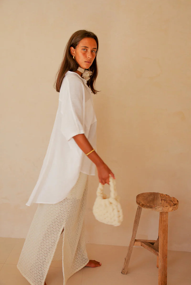 Woman in a white outfit holding a small bag against a beige background
