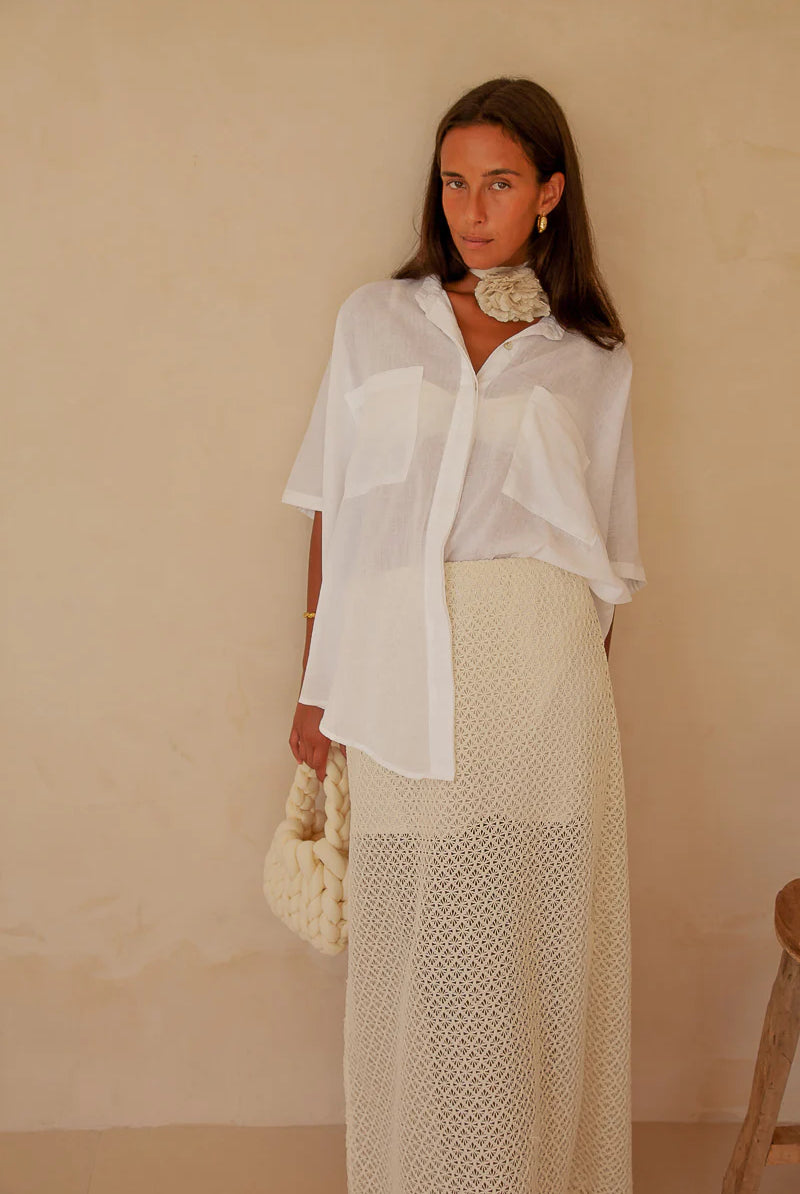 Woman wearing a white blouse and beige skirt against a plain background