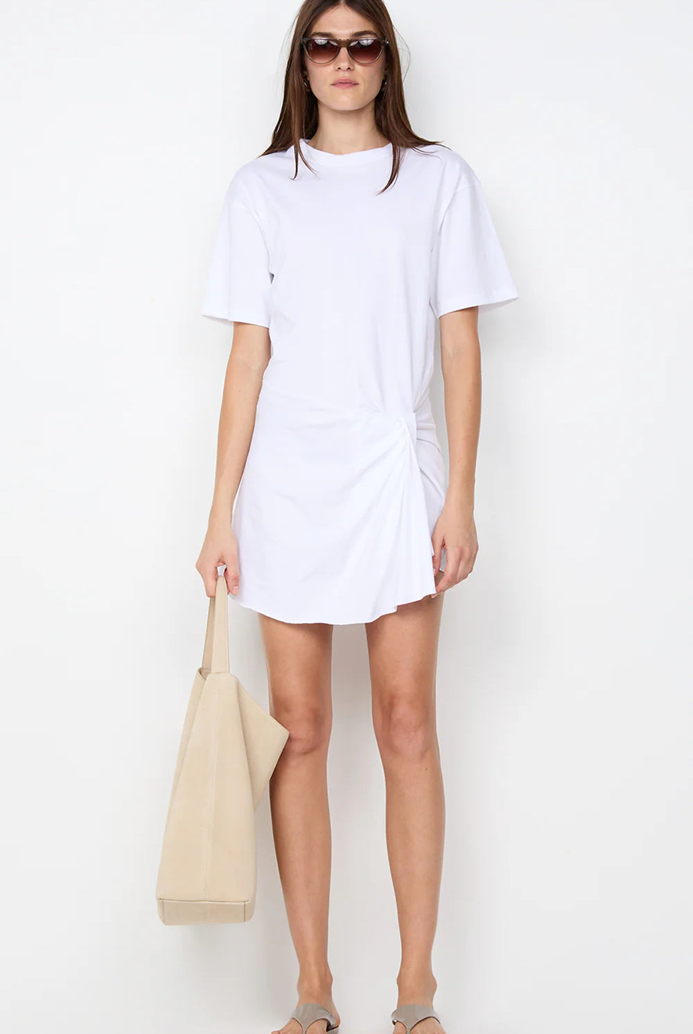 Woman wearing a white t-shirt dress holding a beige bag on a white background