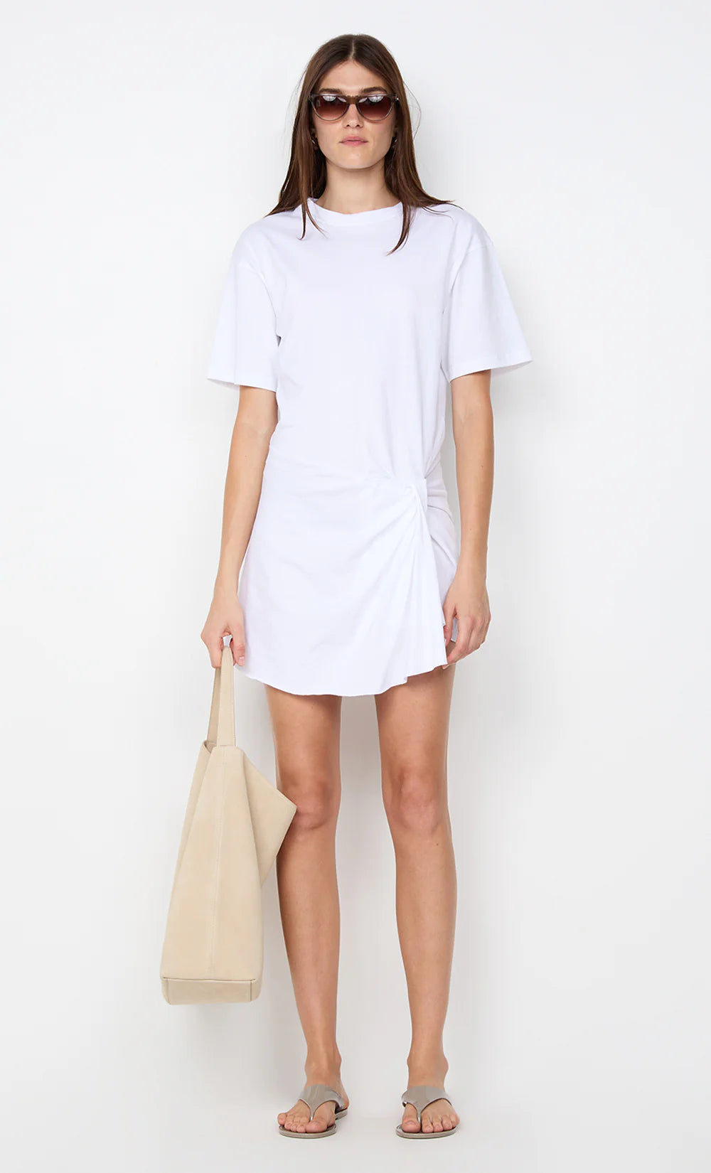 Woman wearing a white t-shirt dress holding a beige bag on a white background