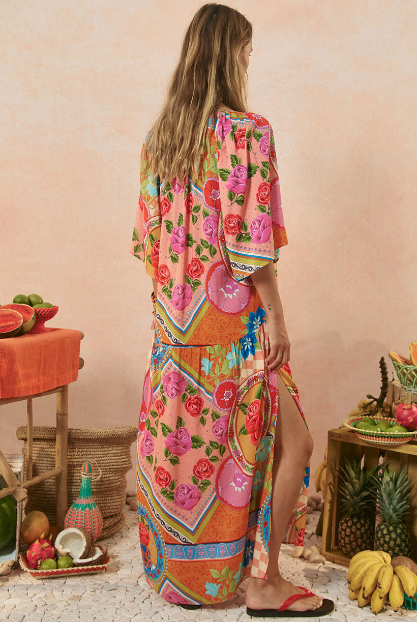 Woman wearing a colorful floral dress standing in a tropical setting with fruits and plants.