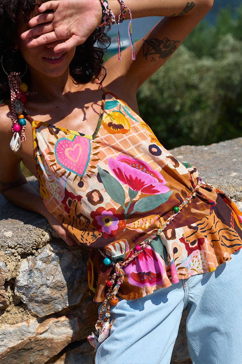 Person wearing a colorful patterned top with floral designs, sitting on rocks outdoors.
