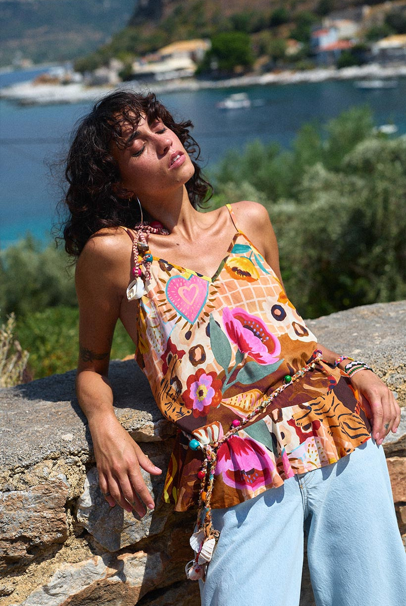 Woman wearing a colorful patterned top with a scenic background of water and greenery.
