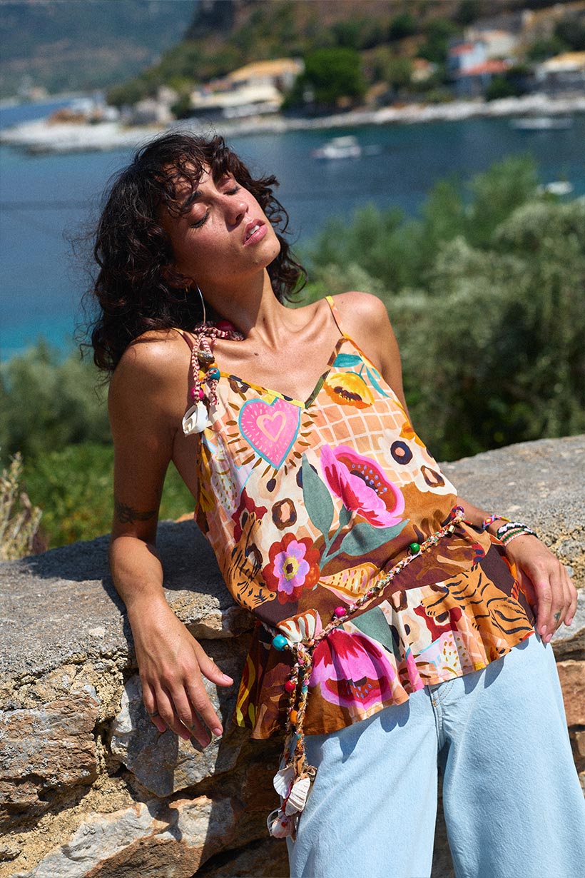 Woman wearing a colorful patterned top with a scenic background of water and greenery.