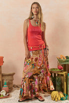 Woman wearing a red tank top and colorful patterned skirt in a rustic setting with fruits and decor.